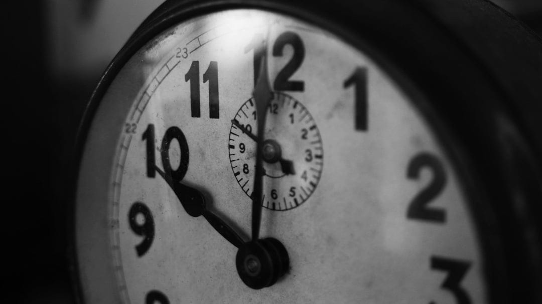 Vintage clock hands point toward ten o'clock on a black and white analog dial with bold, raised Arabic numerals.