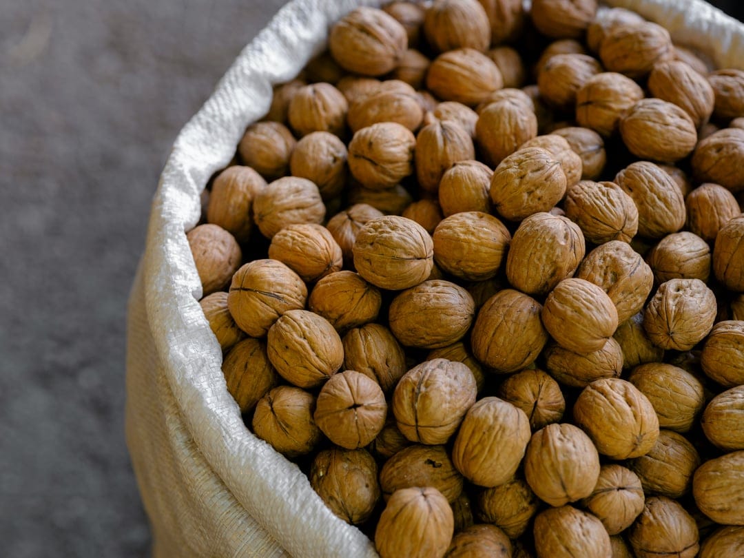 Whole walnuts with ridged brown shells packed inside a coarse white fabric bag under soft top lighting.