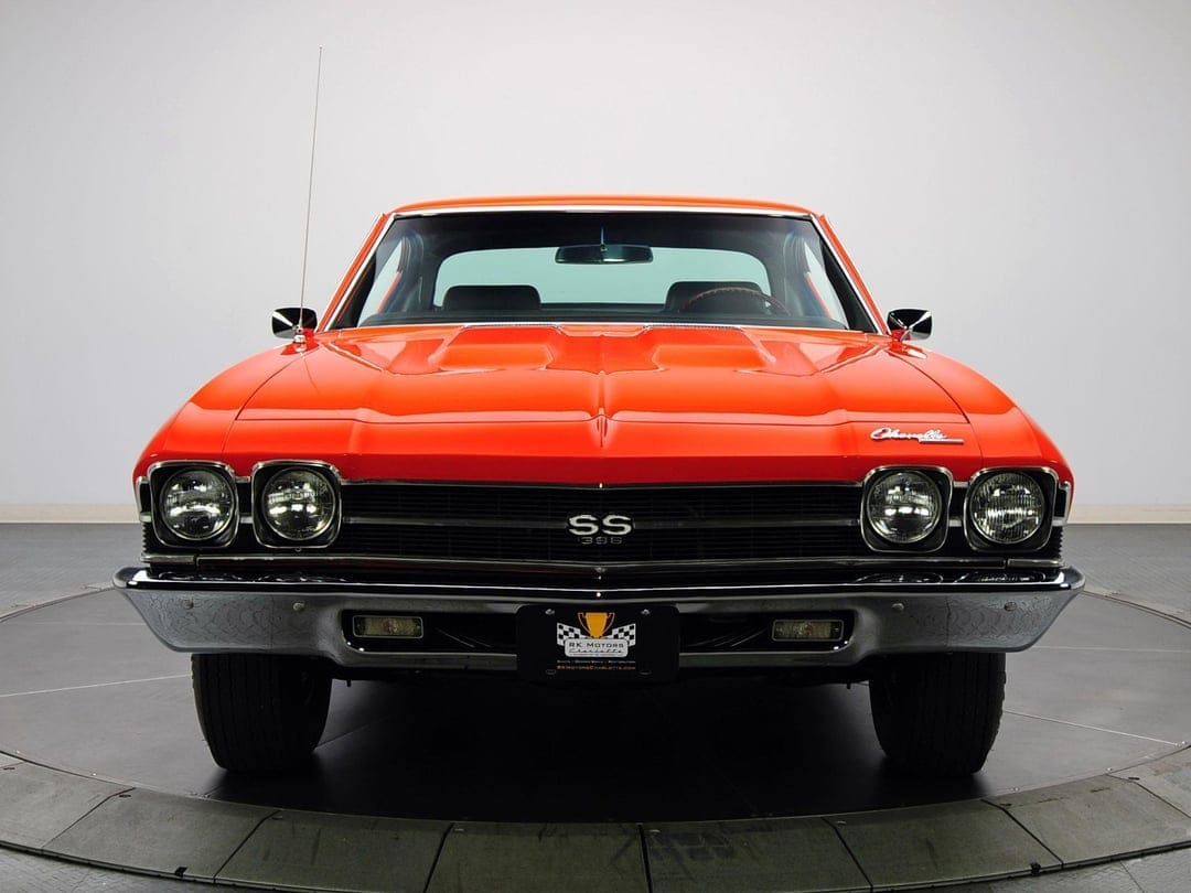Front view of a bright orange 1969 Chevrolet Chevelle SS 396 with chrome trim and black grille in a studio.
