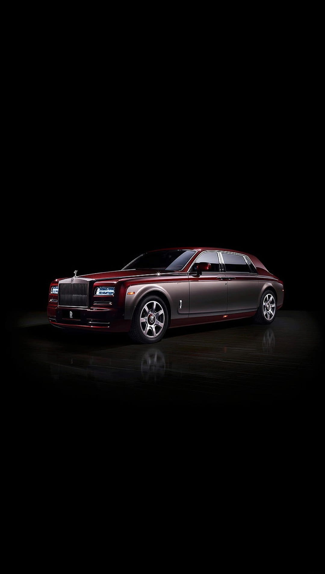Rolls-Royce Phantom luxury sedan with crimson and silver two-tone exterior and glowing headlights in a dark studio.