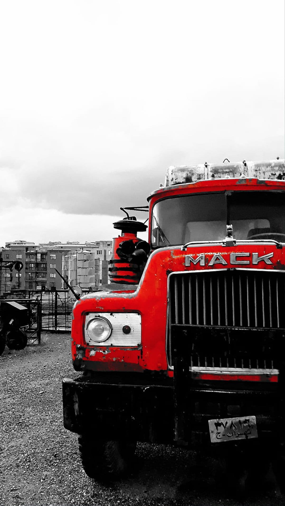 Red Mack truck with a chrome grille and weathered paint parked in a grayscale urban industrial environment.