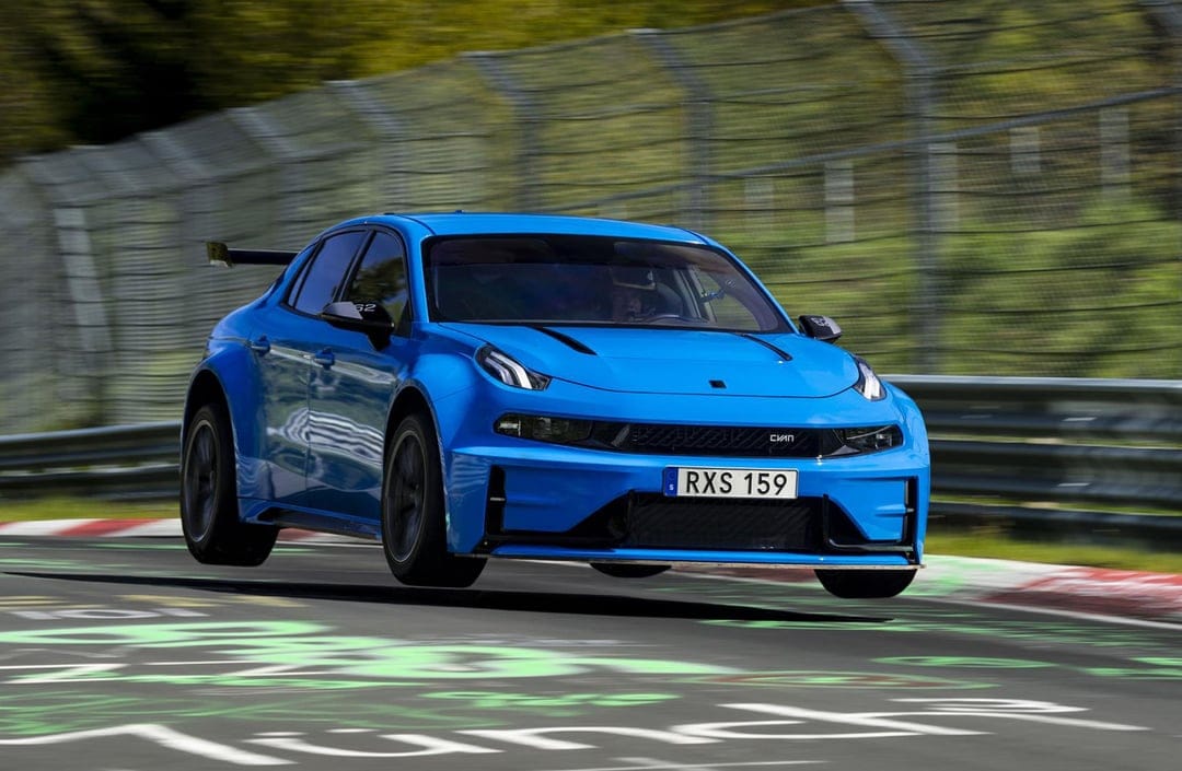 Blue Cyan Racing sedan jumping on a graffiti-covered racetrack with blurred trees and fencing in the background.