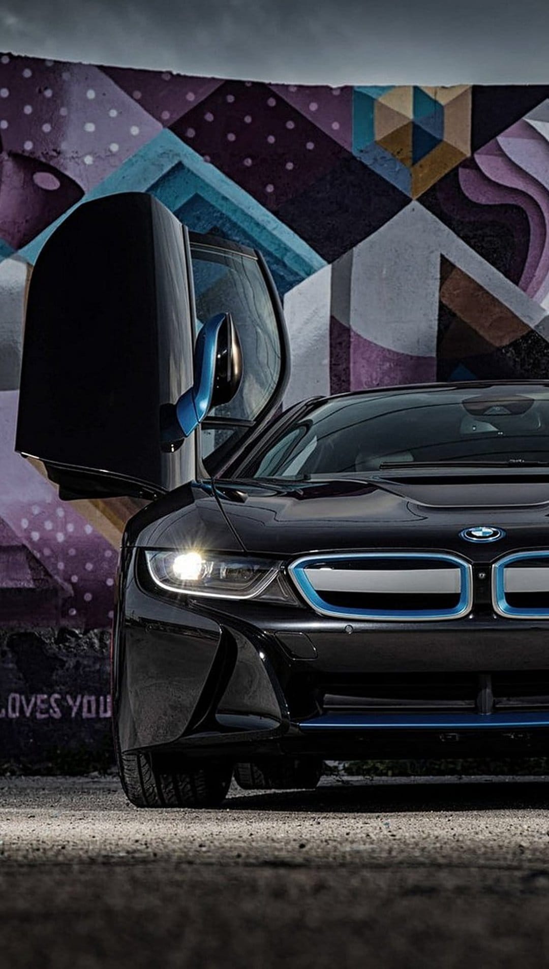 Black BMW i8 with open dihedral doors parked against a purple and blue abstract graffiti wall in a city alley.