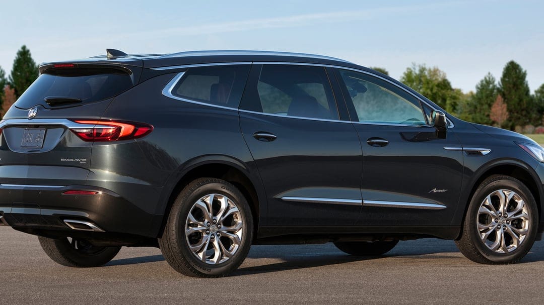 Dark gray Buick Enclave Avenir SUV with chrome trim and alloy wheels on asphalt under a clear blue sky.