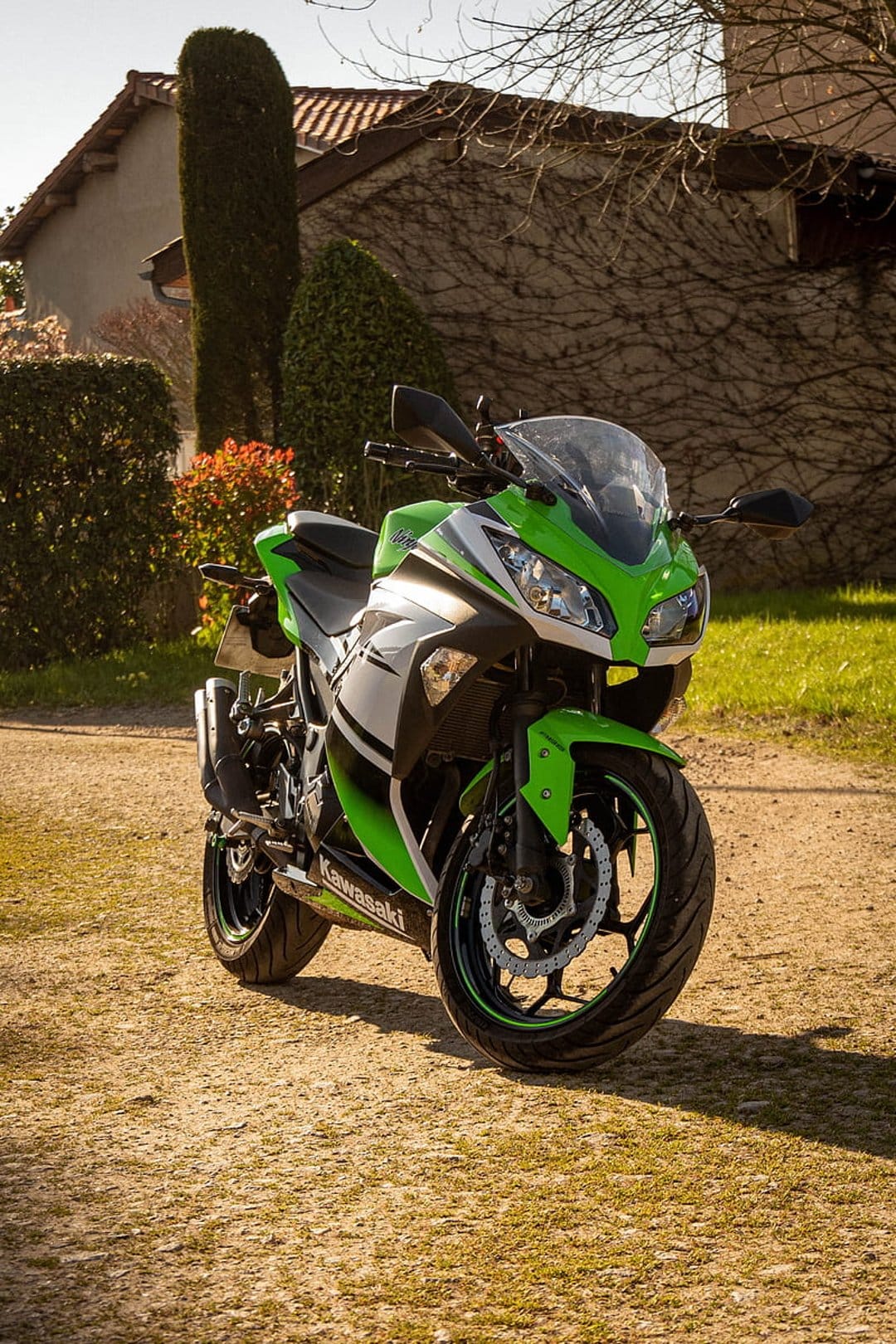 Kawasaki Ninja sportbike in lime green parked on a dirt path beside an ivy-covered stone building in sunlight.