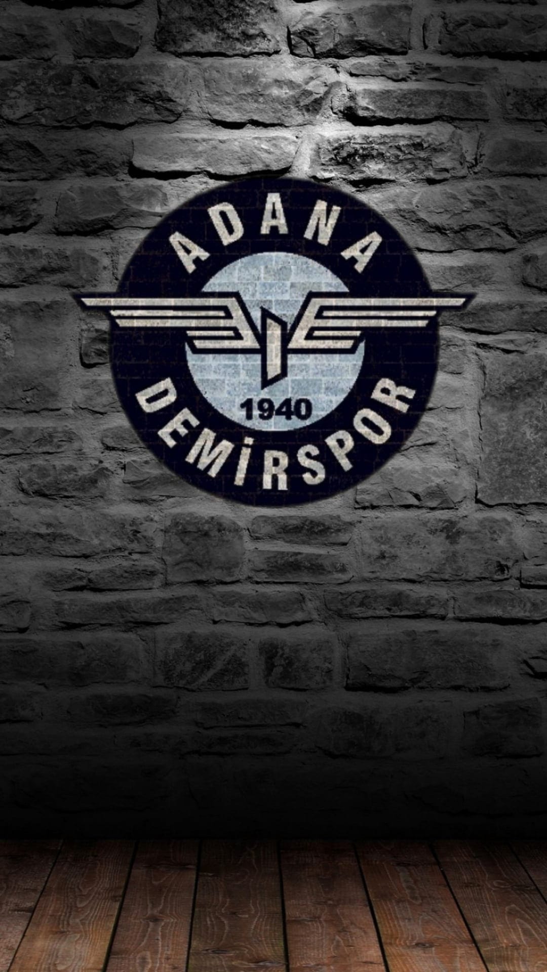 Adana Demirspor 1940 logo with wings on a dark gray brick wall above a rustic wooden floor with moody shadows.