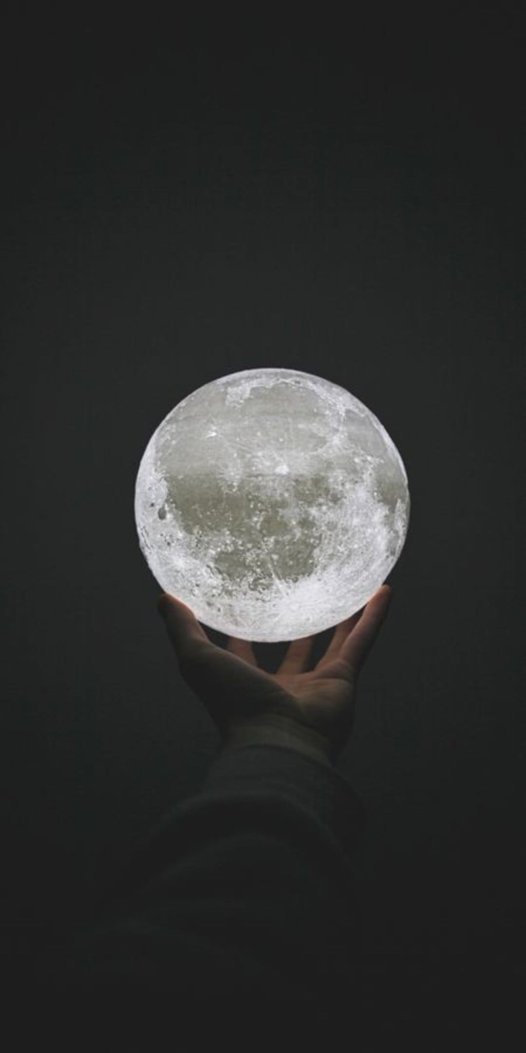 Human hand cradles a realistic glowing moon lamp with detailed craters against a solid black background.