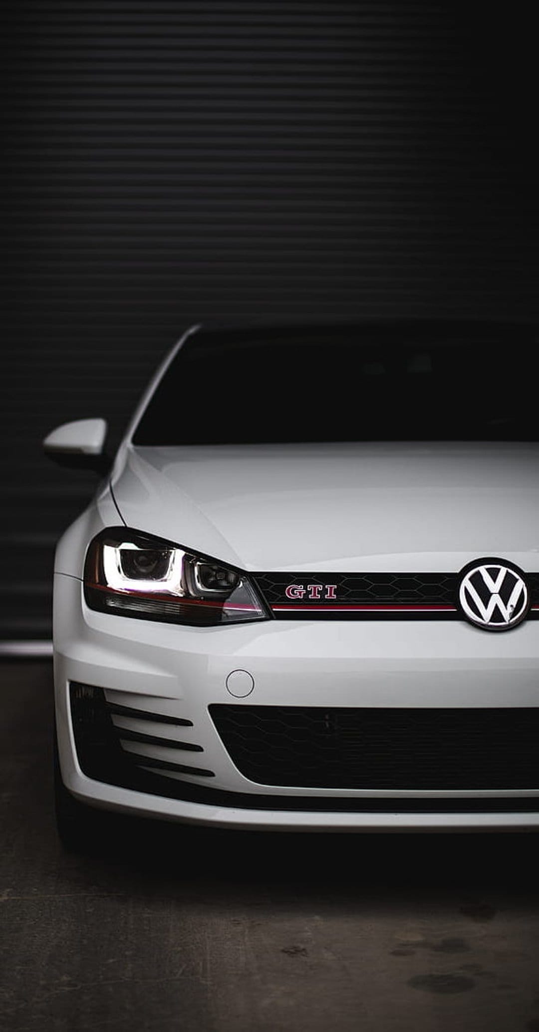 White Volkswagen Golf GTI front grille with red trim, LED headlights, and badge against a dark textured backdrop.