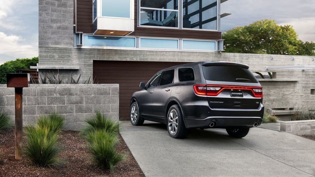 Rear view of a charcoal Dodge Durango SUV on a driveway in front of a modern house with concrete and glass walls.