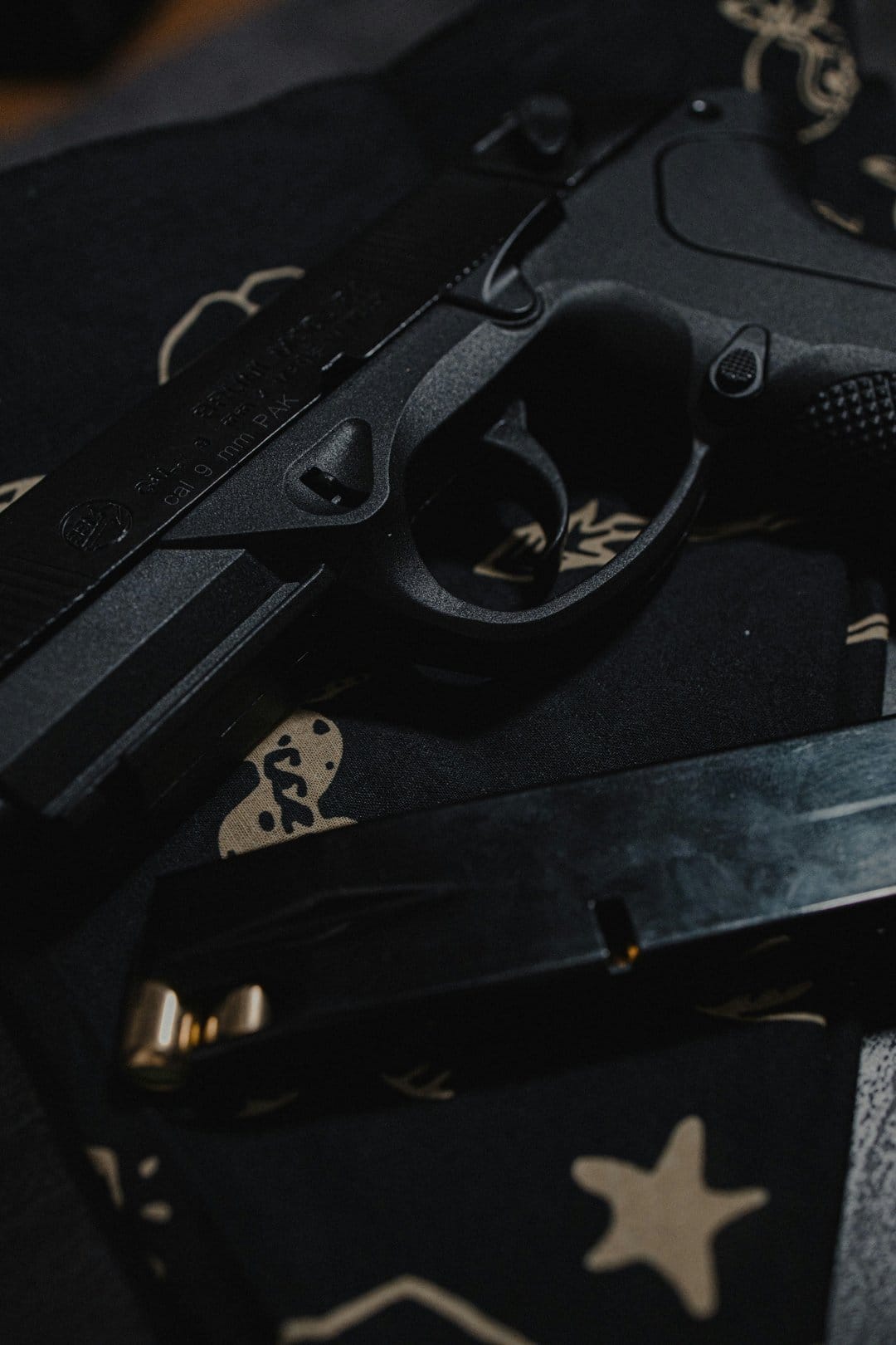 Black semi-automatic pistol and loaded magazine on dark fabric with beige star patterns and visible brass bullets.