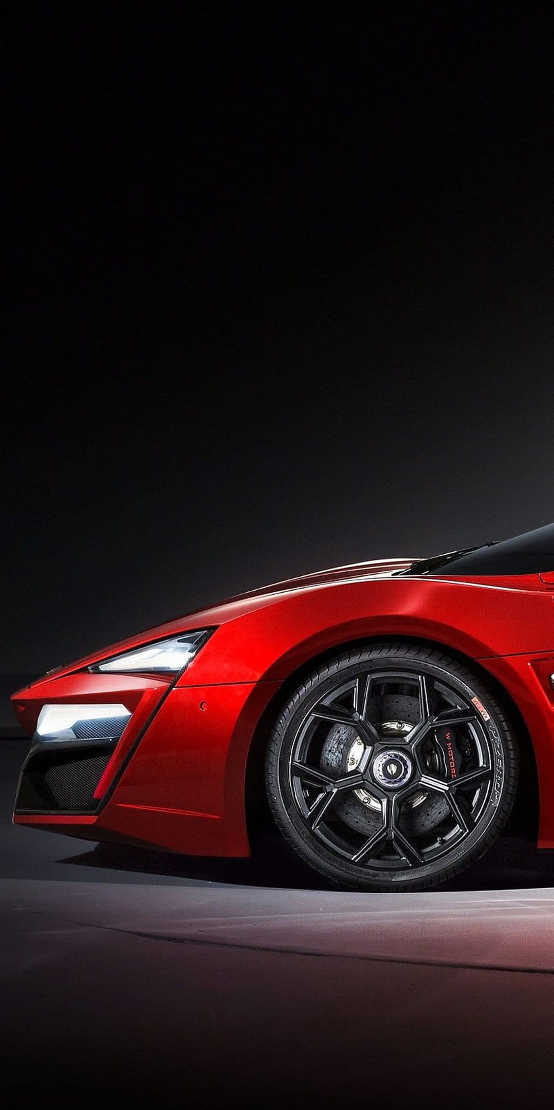 Red sports car fender featuring illuminated LED headlights, a black geometric alloy rim, and brake calipers.