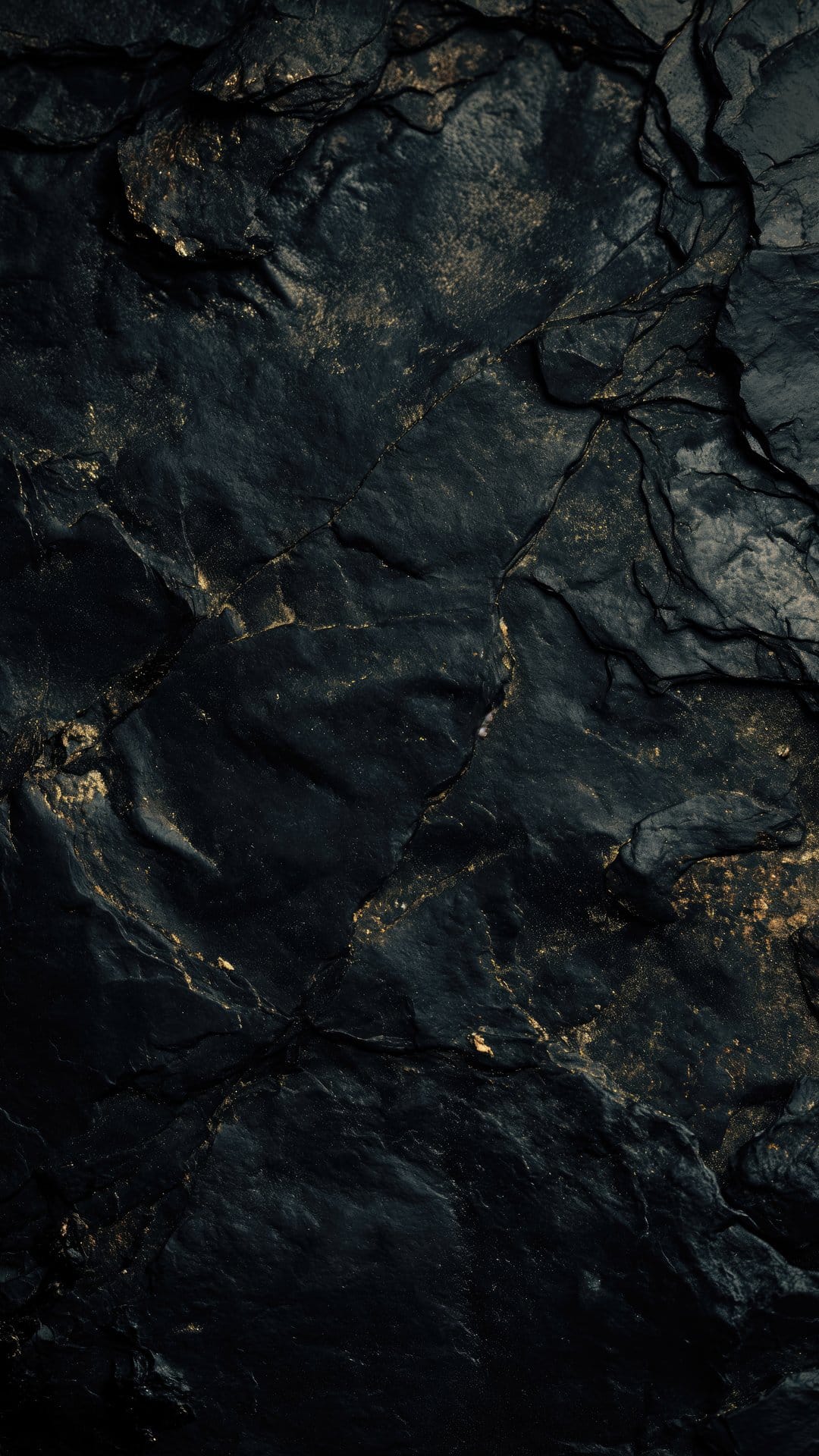 Gold veins and metallic flecks embedded in a dark, jagged obsidian rock surface with deep shadows and cracks.