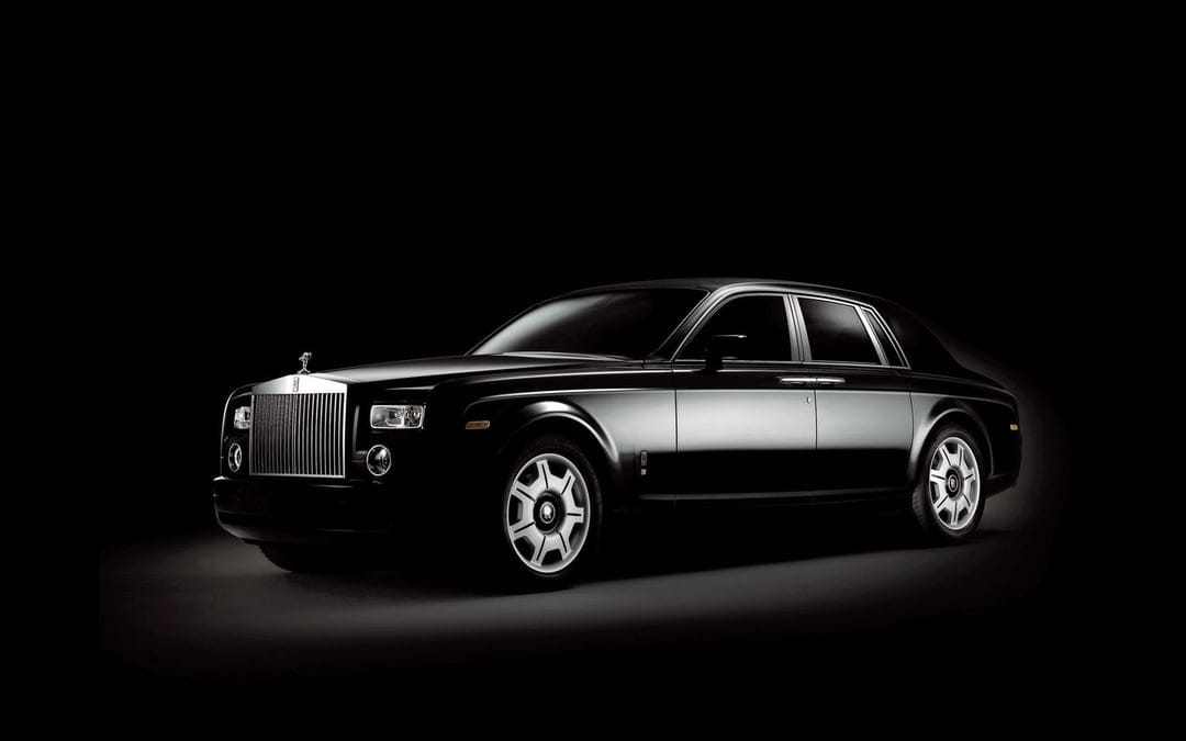 Black Rolls-Royce Phantom sedan in a dark studio with chrome accents and silver wheels on a black background.