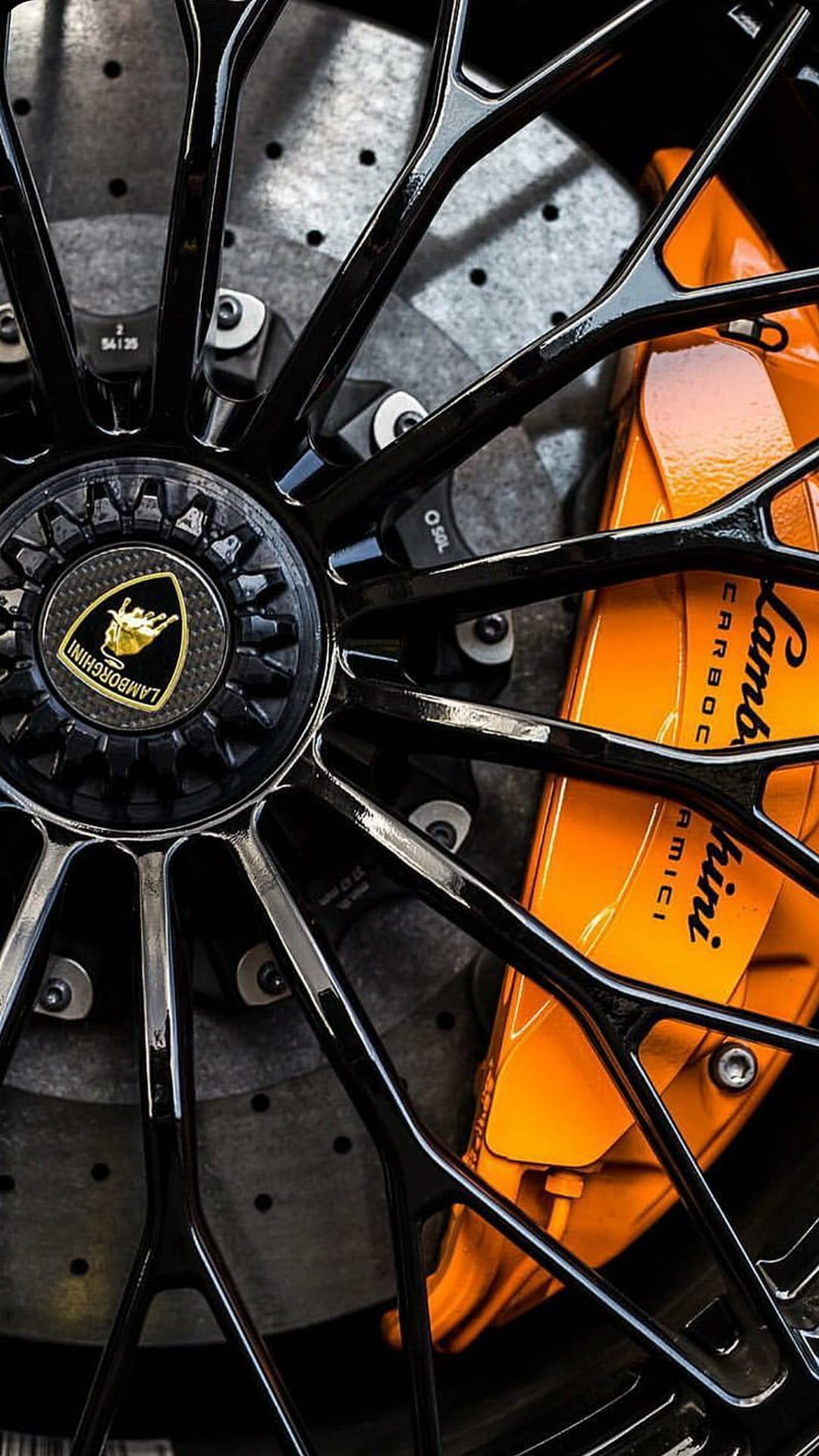 Lamborghini black alloy rim spokes and an orange carbon ceramic brake caliper with white branding text.