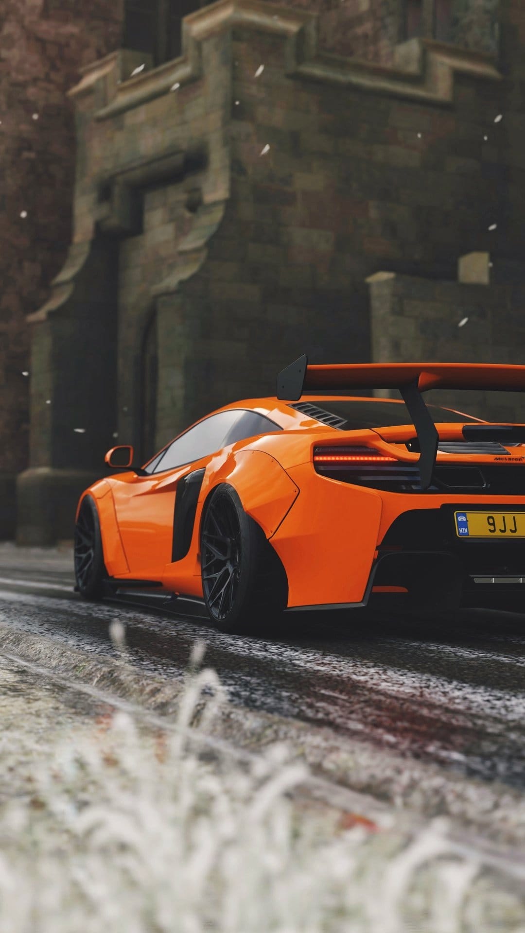 Orange McLaren supercar with a rear spoiler driving on a wet snowy road past ancient stone buildings.