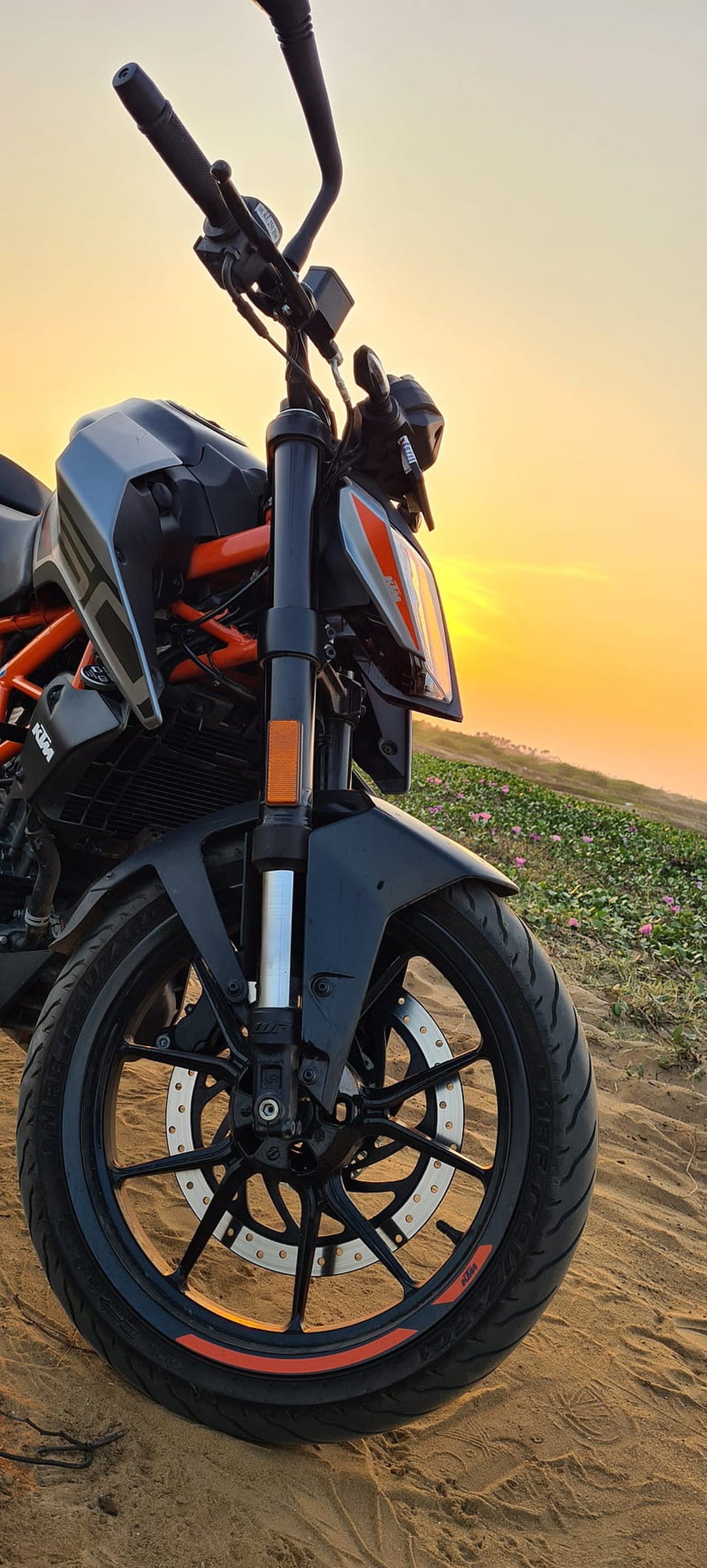 Black KTM Duke motorcycle with orange accents parked on a sandy beach under a warm sunset glow.