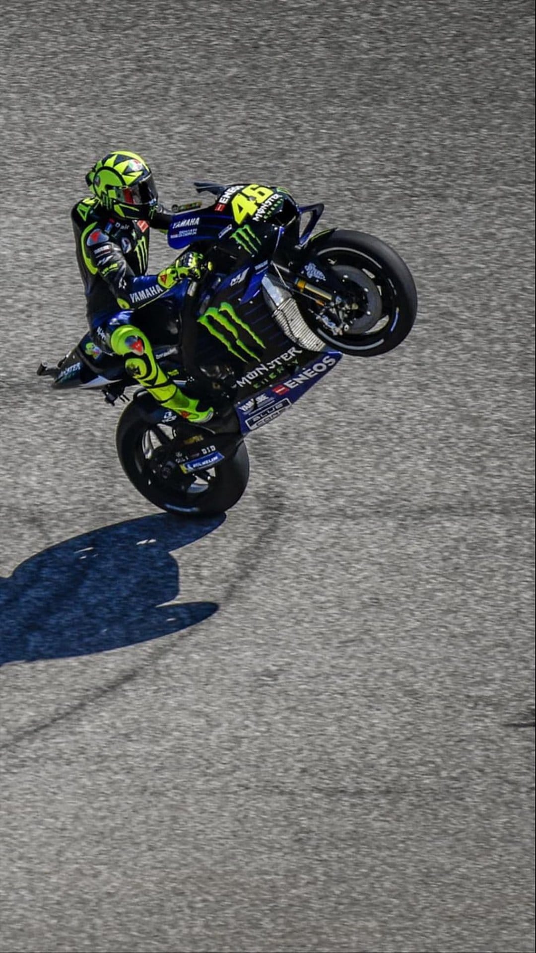 Valentino Rossi performs a wheelie on a Yamaha MotoGP bike while wearing a yellow and black racing suit.