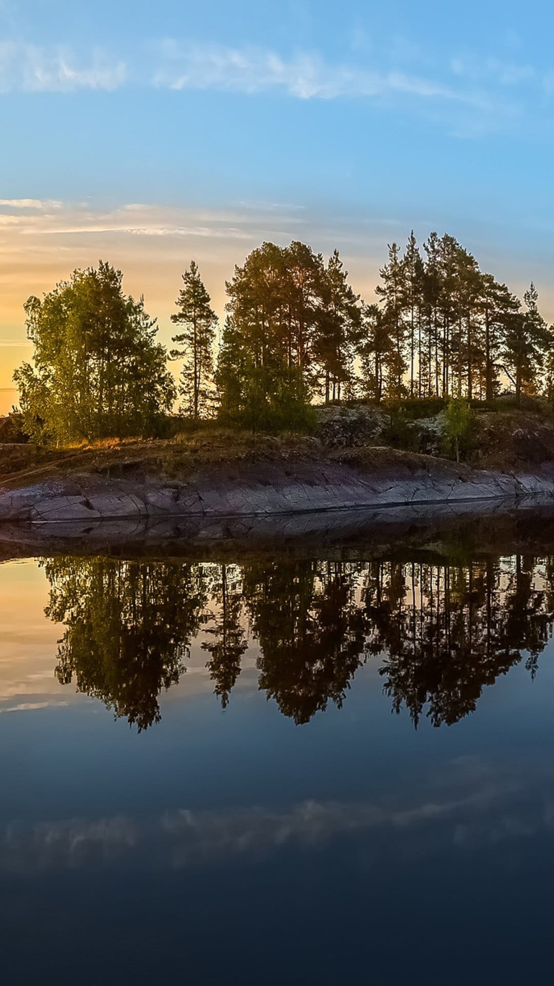 Silhouetted trees reflect onto a calm lake during a vibrant blue and orange sunset in a vertical landscape.