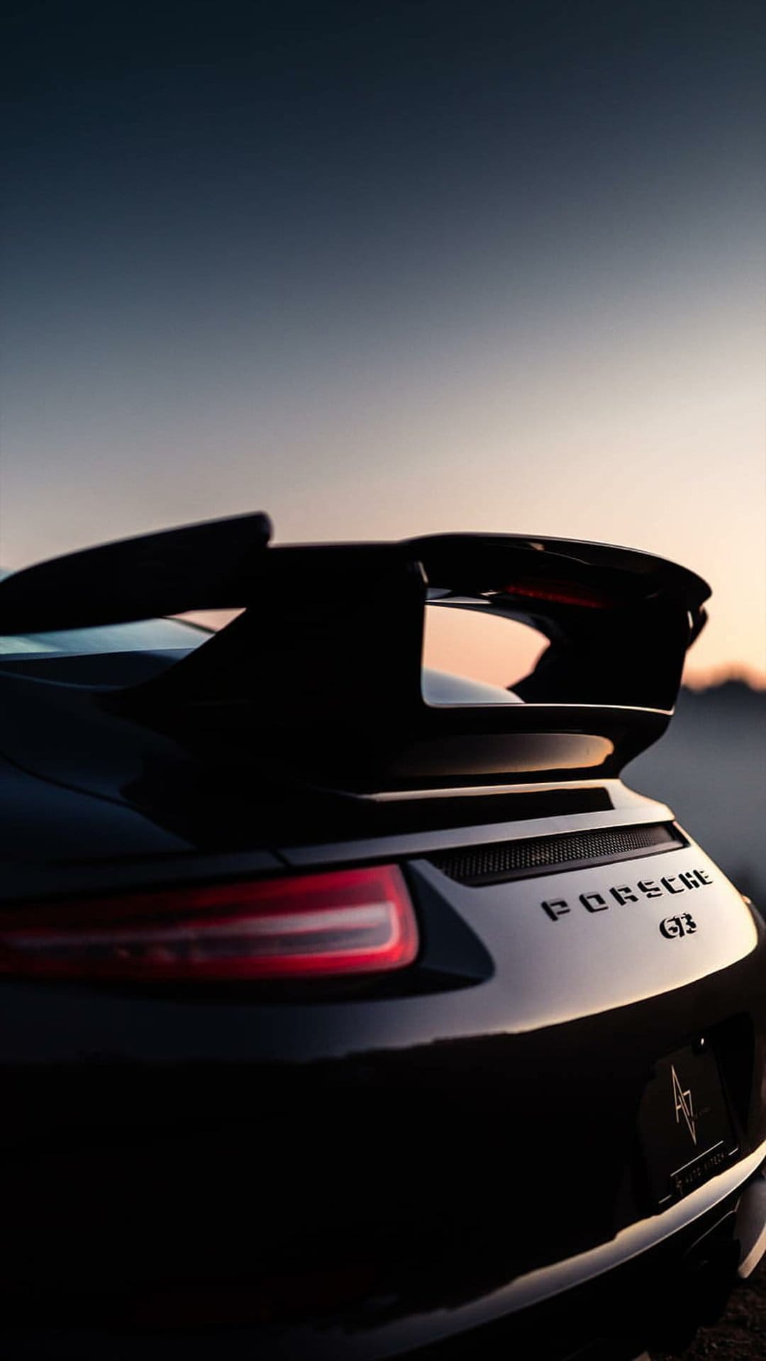 Porsche GT3 rear wing and silver badging catch the warm sunset light against a polished black metallic body.