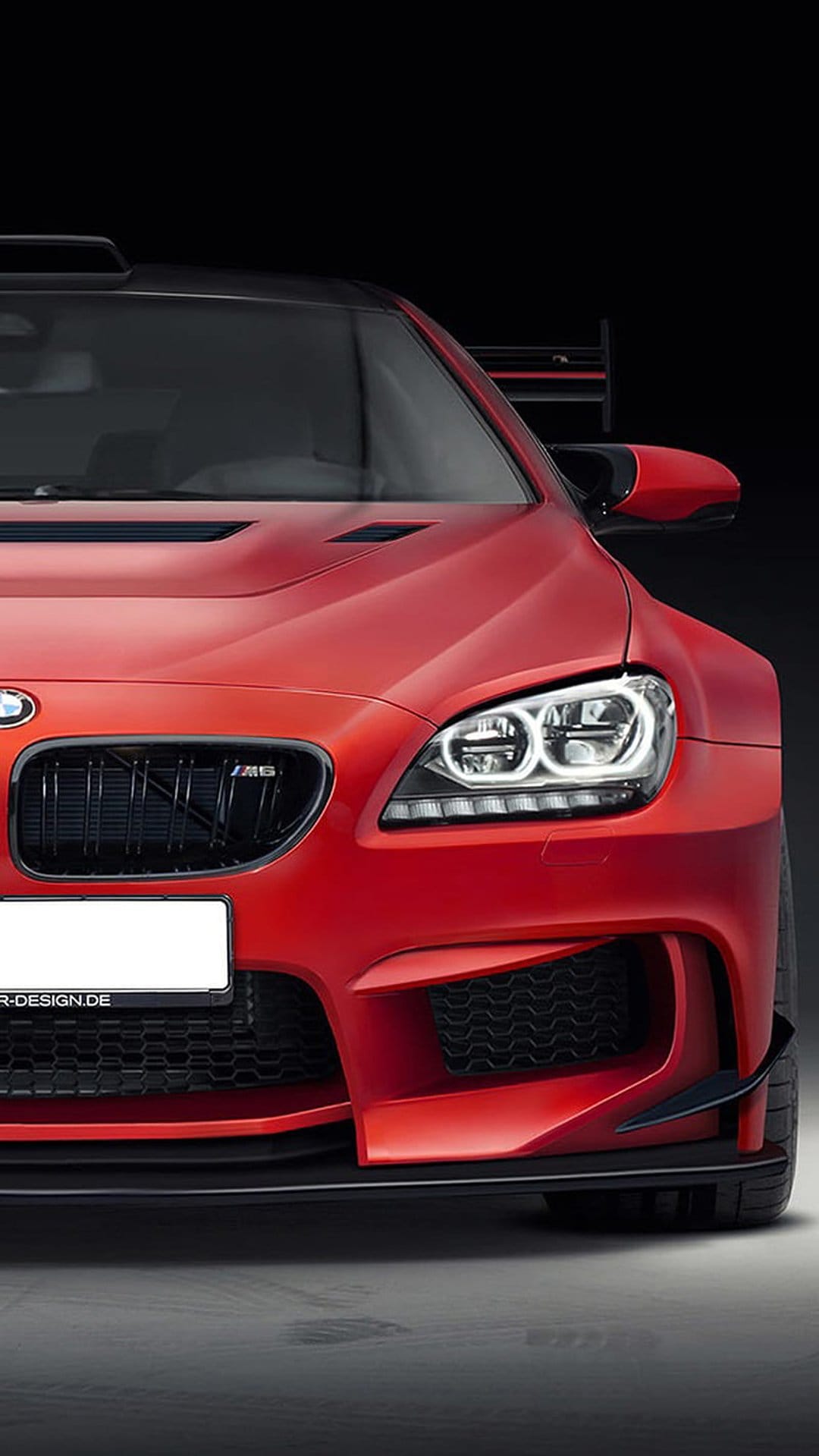 Red BMW M6 coupe featuring LED headlights and a black grille against a dark, shadowy studio background.
