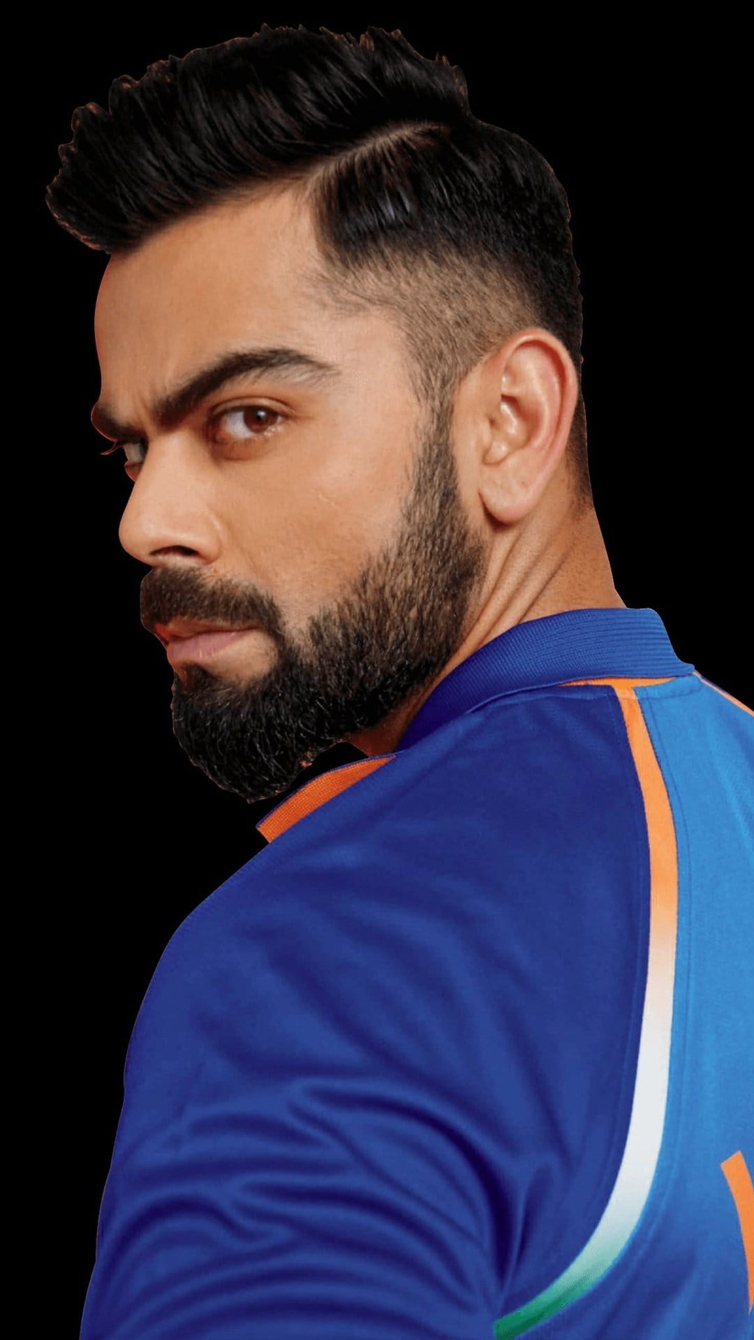 Virat Kohli looking over his shoulder while wearing a blue Indian cricket jersey with a groomed beard and styled hair.