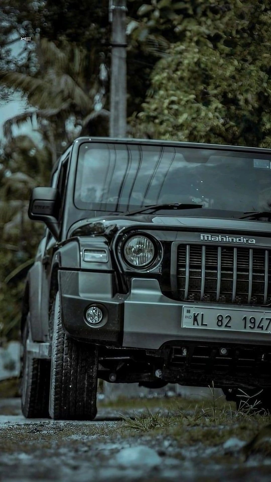 Mahindra Thar SUV with round headlights parked on a jungle trail surrounded by dense green leaves and forest trees.