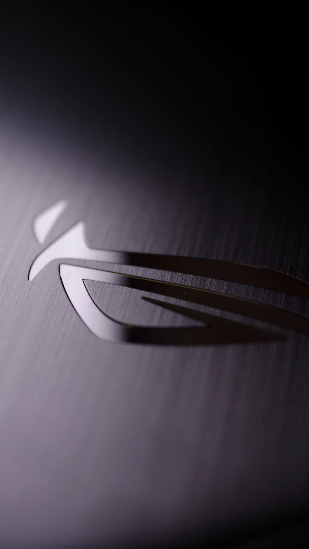 ROG logo engraved on a dark brushed metal surface with a soft light gradient across the industrial texture.