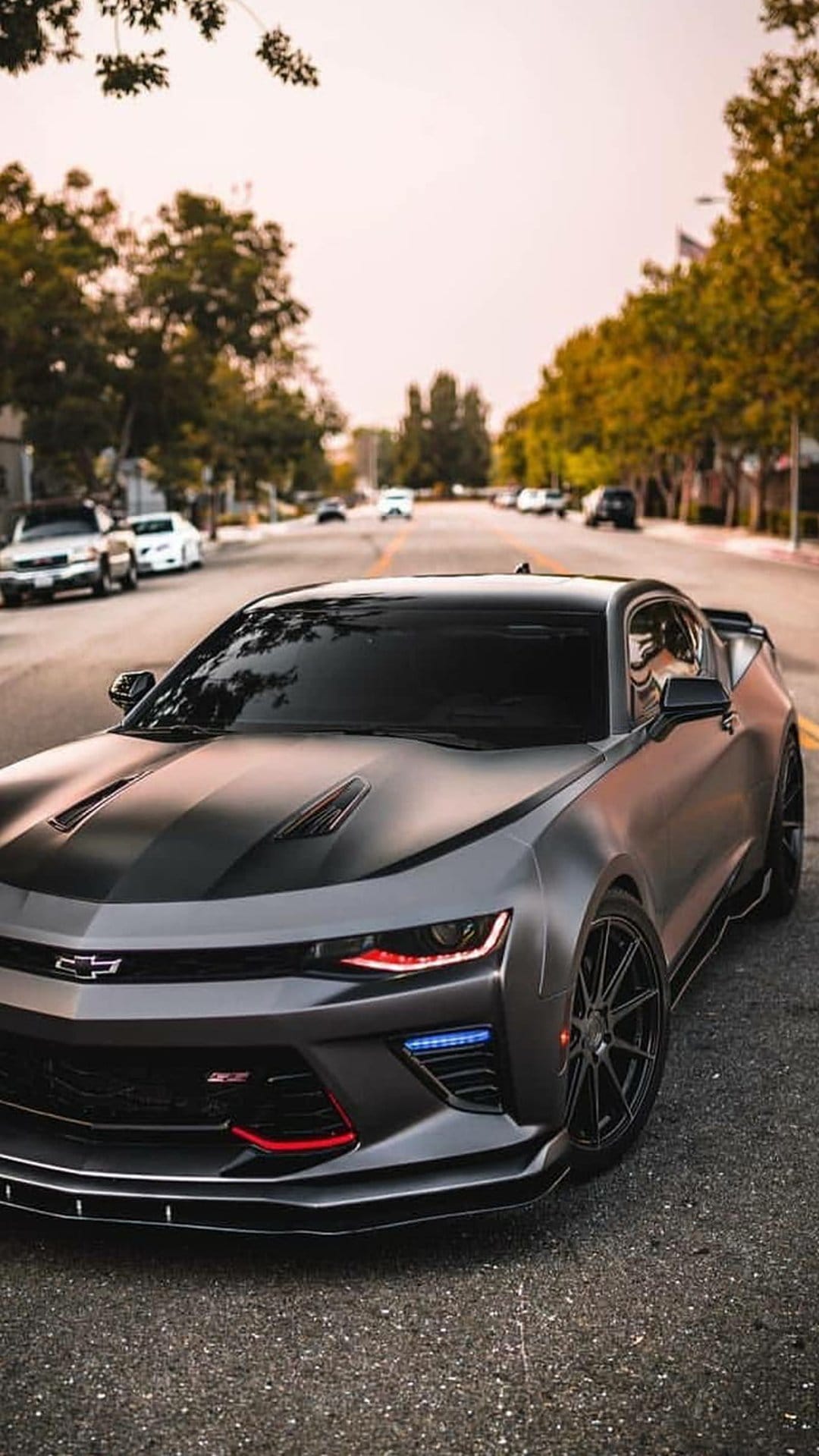 Matte black Chevrolet Camaro ZL1 with red and blue accents parked on a tree-lined street at a low angle.