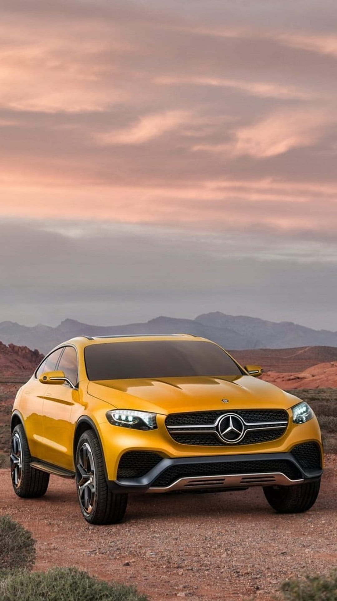 Yellow Mercedes SUV concept car parked on a sandy desert road with jagged mountains under a soft twilight sky.