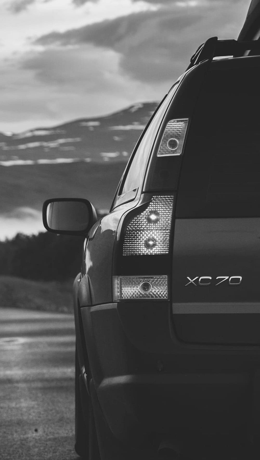 Volvo XC70 rear tail light and badge detail set against a blurred background of mountains and cloudy sky.
