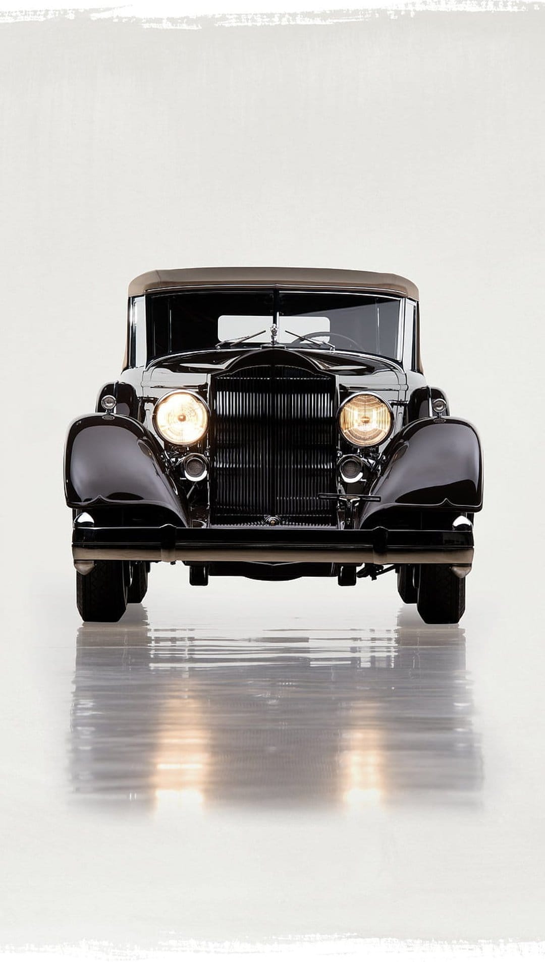 Vintage black convertible car with a tall chrome grille, round headlights, and a brown fabric top in a studio.