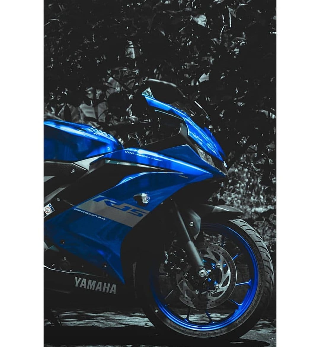 Yamaha R15 motorcycle in electric blue showcases front fairing and brake disc against a dark foliage background.