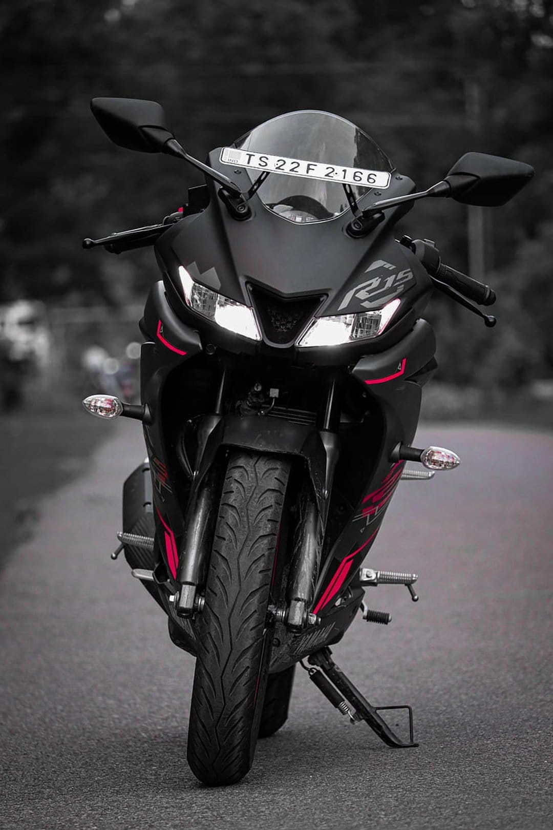 Yamaha R15 sportbike in matte black with red accents and illuminated headlights against a soft blurred background.