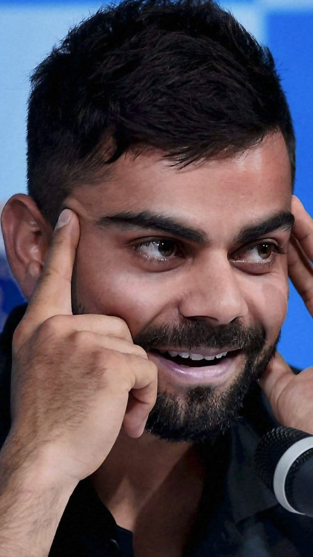 Virat Kohli touches his temple with a contemplative expression, showcasing his dark beard and focused brown eyes.