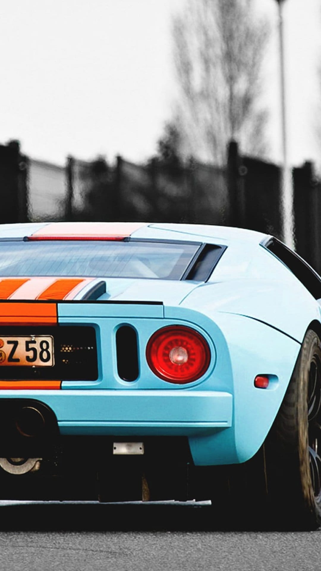Ford GT rear taillight and orange racing stripes on powder blue bodywork in a vertical automotive close-up.
