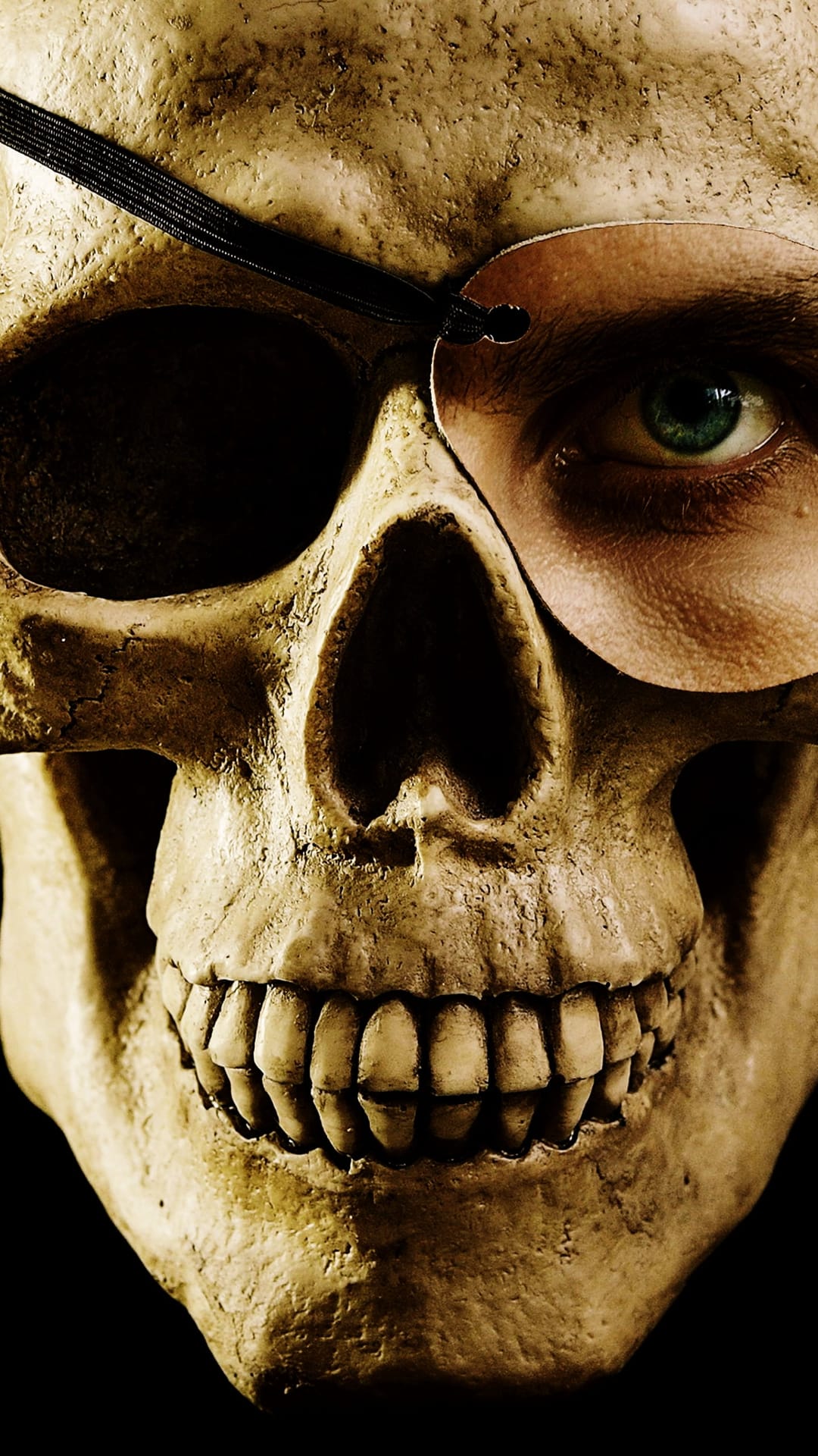 Weathered skull wearing a black leather eye patch with a single piercing green human eye staring from the socket.
