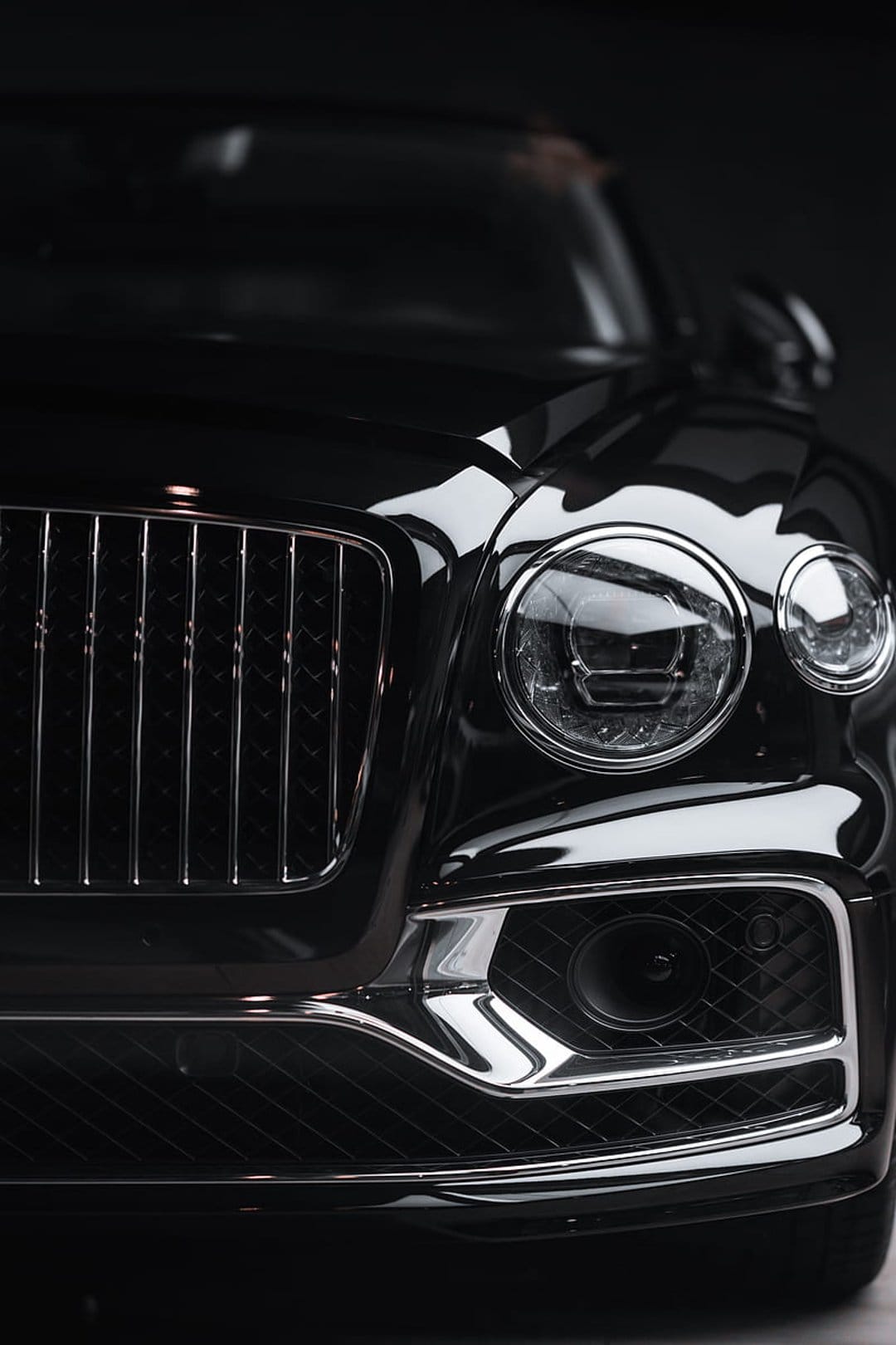 Black Bentley Continental GT front view featuring a chrome lattice grille and round LED headlights in close-up.