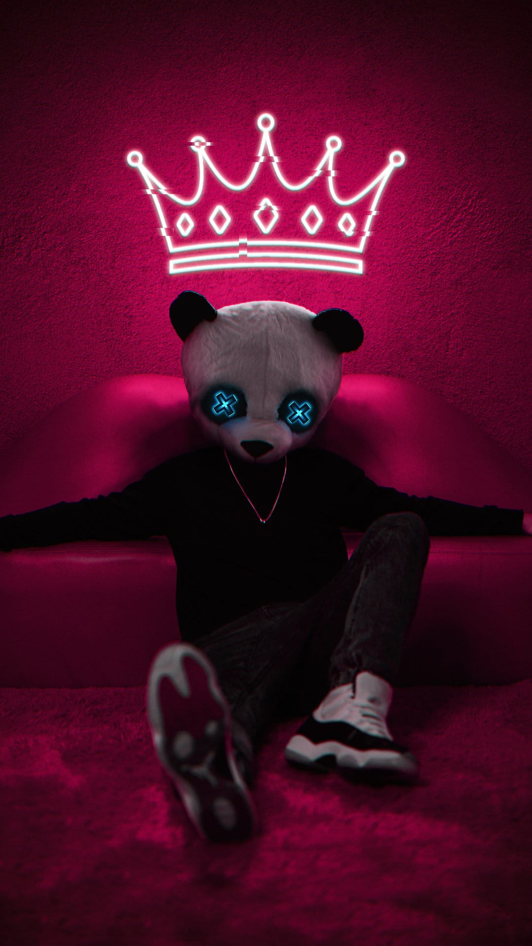 Panda mask with glowing blue eyes and a neon crown sits on a couch wearing black streetwear against pink.