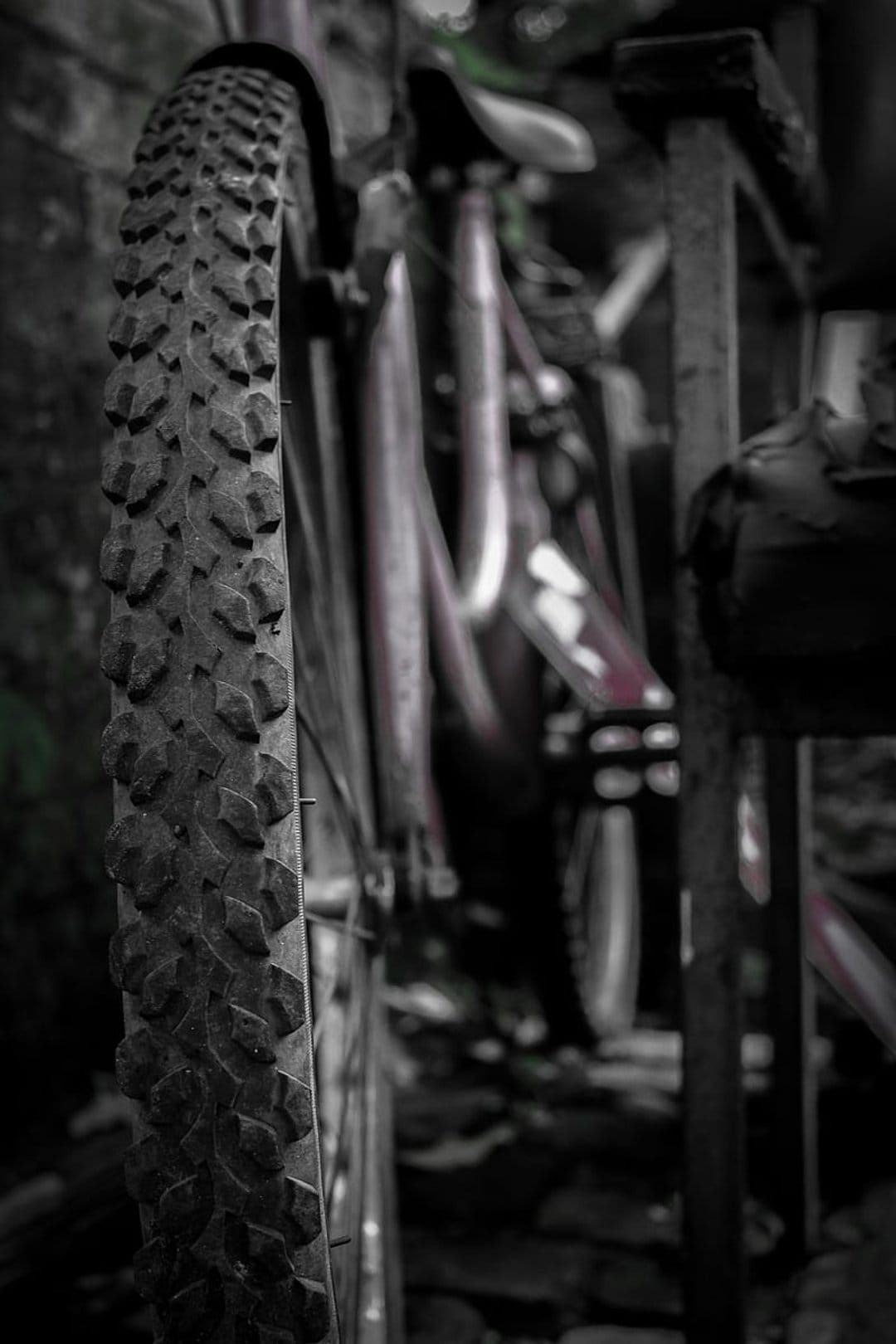 Mountain bike tire with deep tread patterns appears in sharp focus against a blurred frame and handlebar background.