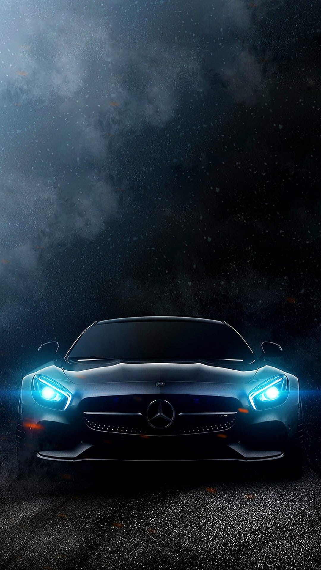 Mercedes-AMG GT S with glowing blue headlights on damp night asphalt, focused on the front grille and emblem.