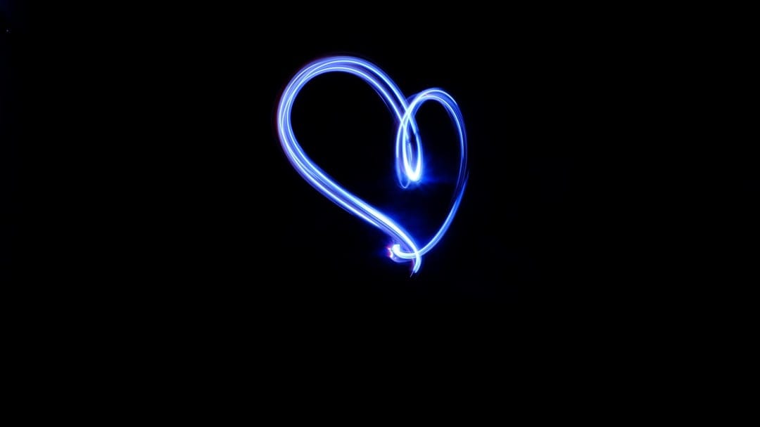 Blue neon light trails forming a heart shape against a solid black background in a vertical composition.