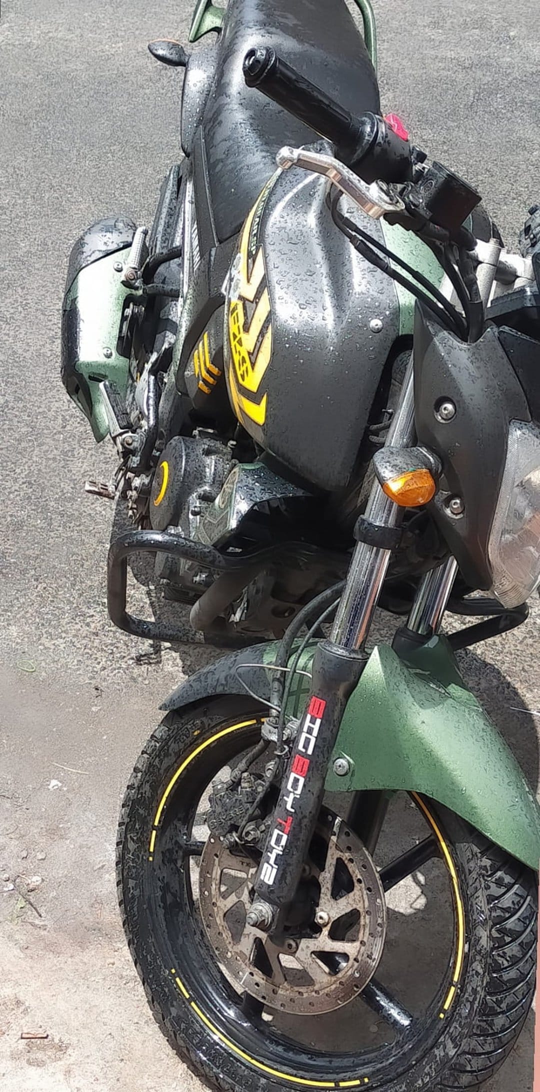 Green motorcycle with yellow stripes and water droplets on the fuel tank, featuring a front disc brake and tire.