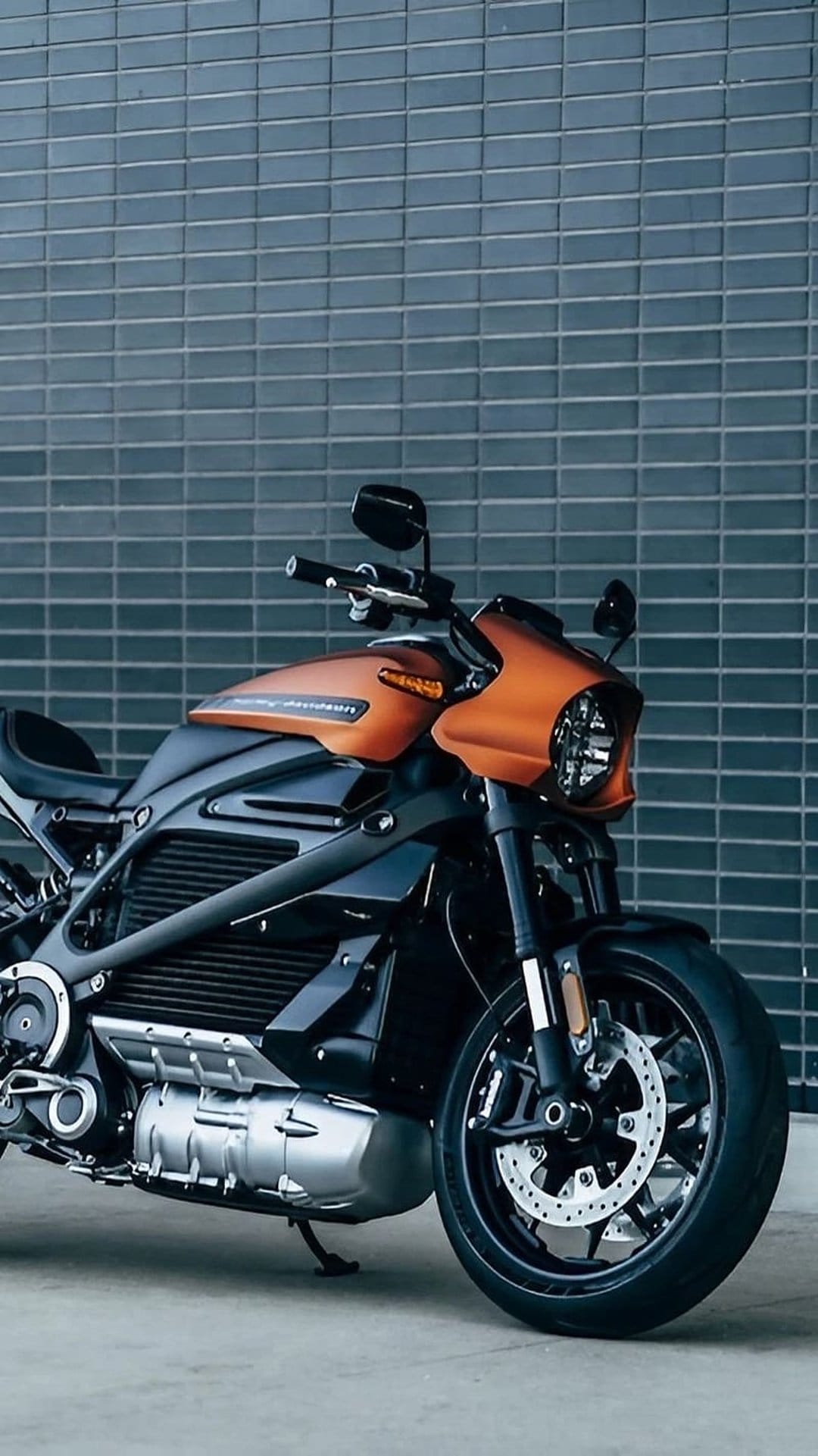 Harley-Davidson LiveWire electric motorcycle with orange bodywork and an LED headlight against a dark brick wall.