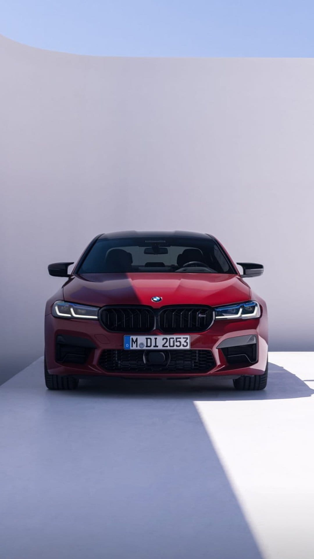 Red BMW M5 sedan with a black grille and glowing LED headlights centered on a minimalist white background.