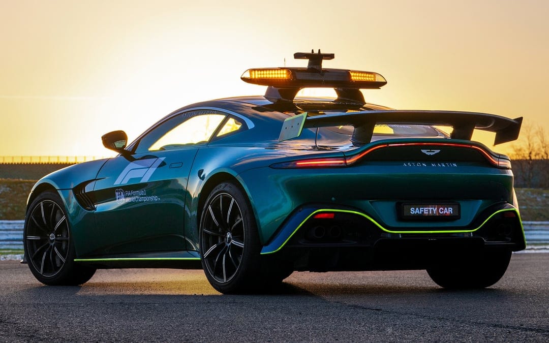 Aston Martin F1 Safety Car in British Racing Green with lit amber lights at sunset on a racetrack.