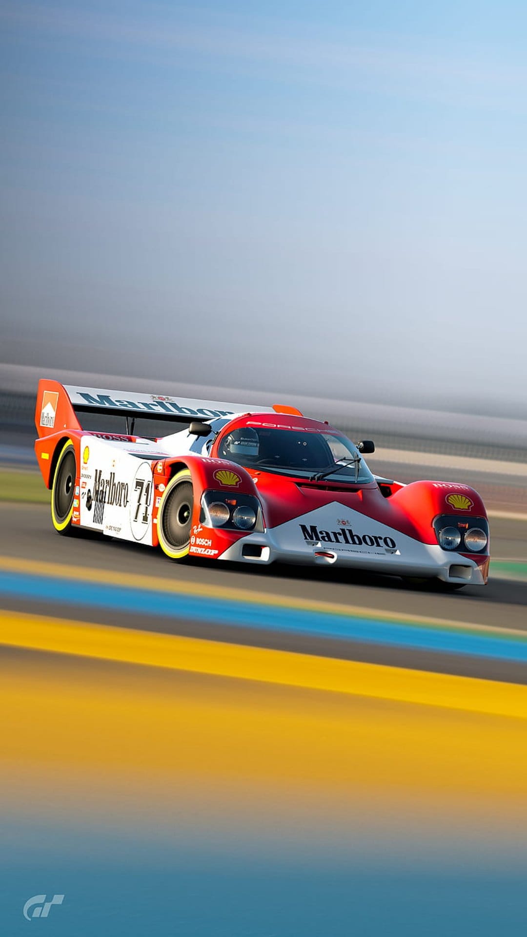 Porsche 962C racing car in red and white livery speeds on a track with motion blur in a portrait orientation.