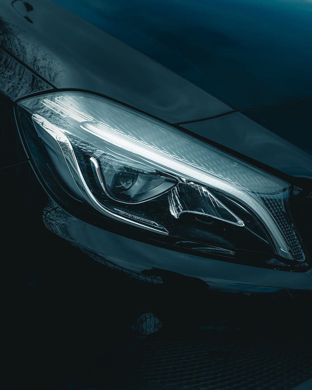 LED car headlight with sharp crystalline optics set against a deep black metallic body panel and chrome accents.