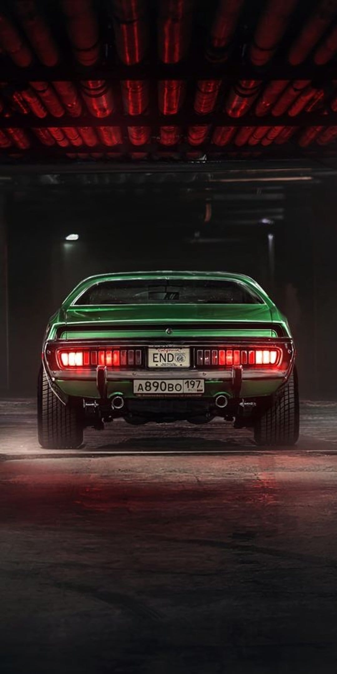 Green muscle car with glowing red taillights and chrome bumpers parked in a dimly lit industrial garage scene.