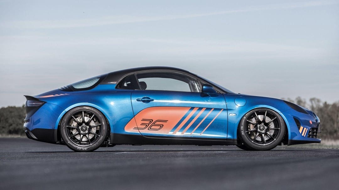 Side profile of a blue Alpine A110 Cup race car with orange graphics and black wheels on a paved track.