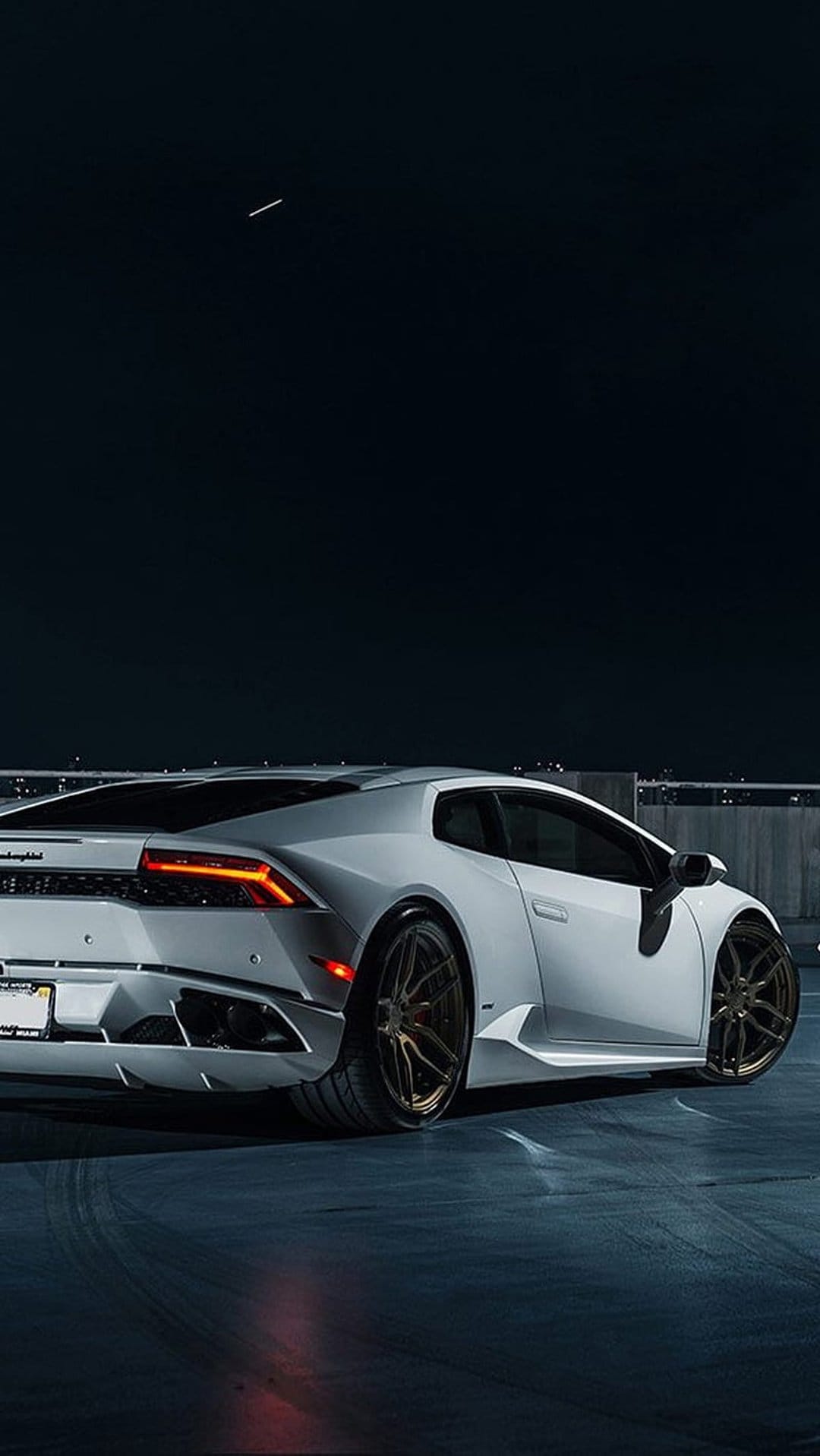 White Lamborghini Huracan rear view with glowing taillights and bronze wheels on dark asphalt at night.